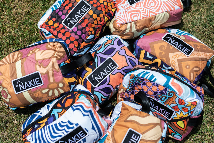 Collection of Nakie toiletry bags with vibrant geometric and patterned designs in orange, purple, blue