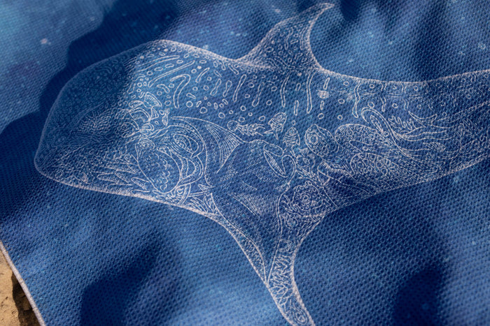 Blue beach towel with intricate white embroidered manta ray and ocean-inspired pattern design