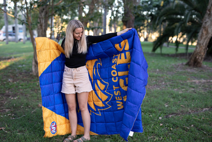 Blue and gold quilted puffy blanket with West Coast Eagles AFL logo, displayed outdoors