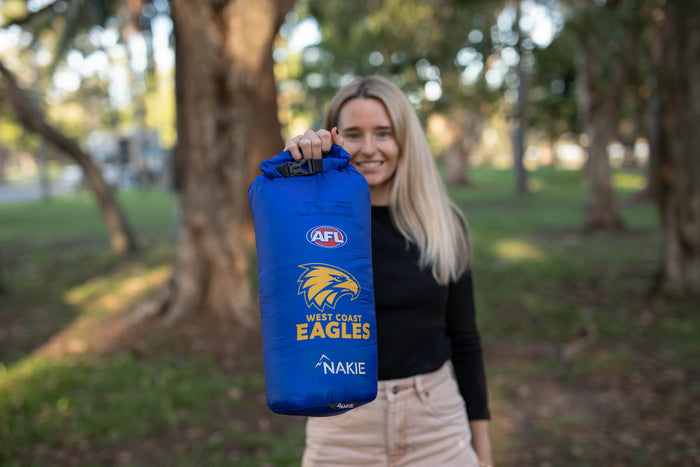 Blue West Coast Eagles AFL dry bag with roll-top closure and yellow eagle logo, held by person outdoors