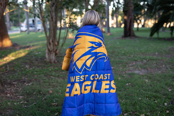 West Coast Eagles blue and gold puffy blanket with eagle logo, worn draped over shoulders outdoors