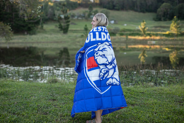Blue Western Bulldogs puffy blanket with white bulldog logo and text, draped over woman's shoulders outdoors