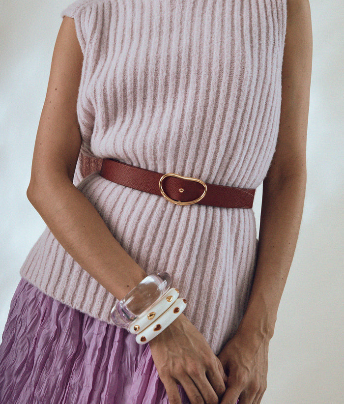 Model wears pink ribbed sweater and skirt with Skinny Georgia Belt in Red and stack of resin cuffs.