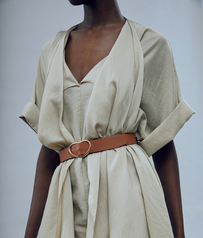 Model on grey backdrop wears tan draped shirt with Wide Georgia Belt in Tan.