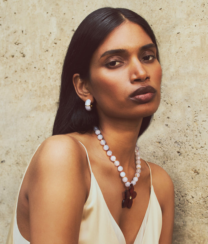Model on tan stone wall wears white cami with Zellige Hoops and Vinca Flower Necklace
