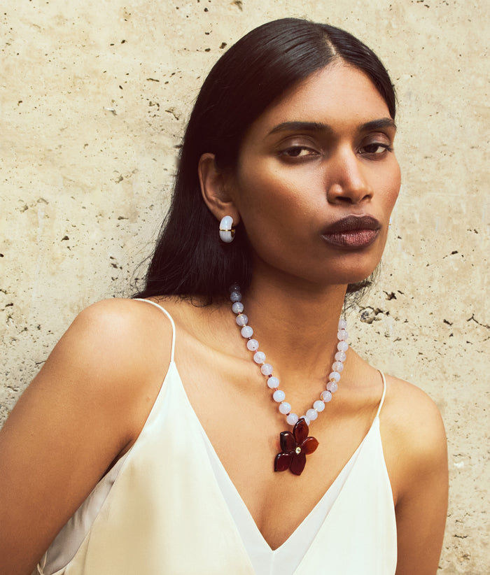 Model on tan stone wall wears white cami with Zellige Hoops and Vinca Flower Necklace, alt view