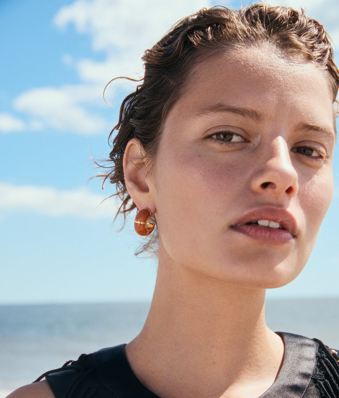 Model face close-up wears black top and Zellige Hoops in Peach Aventurine